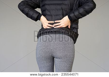 Close-up View Of A Young Woman With Pain In Kidneys Isolated On Gray Background. Young Woman With Ba