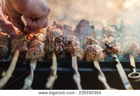 White Man Checks The Availability Of Shish Kebab On A Barbecue Grill Over Charcoal.