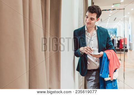 Man in fashion store waiting for his woman to appear from the fitting room being a bit bored