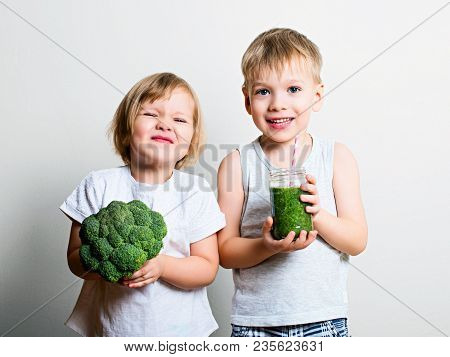 Two Pretty Fun Kids With Green Smoothies And Broccoli Over Grey Background. Helthy And Clean Food Fo