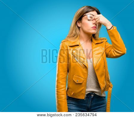 Beautiful young woman with sleepy expression, being overworked and tired, rubbes nose because of weariness, blue background