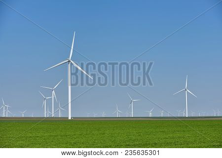 Eolian Farm Renewable Energy In Fresh Green Field Against Clear Blue Sky