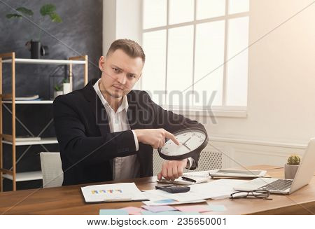 Businessman In Suit Holding Clock And Pointing On It. Portrait Of Man With Watches At Office. Time M