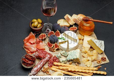 Various Types Of Cheese, Meat, Fruits And Wine On Dark Concrete Background
