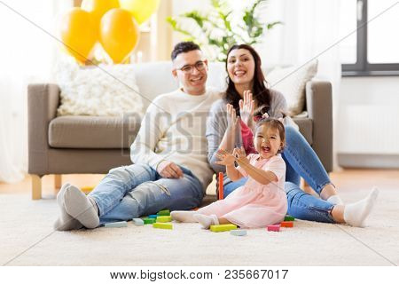 family, holidays and people concept - happy mother, father and little daughter clapping hands at home