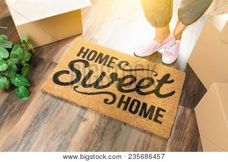 Wman in Pink Shoes and Sweats Standing Near Home Sweet Home Welcome Mat, Boxes and Plant.