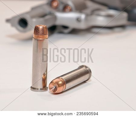 Two Hollow Point 357 Magnum Bullets On A White Table With A Loaded Stainless Revolver In The Backgro