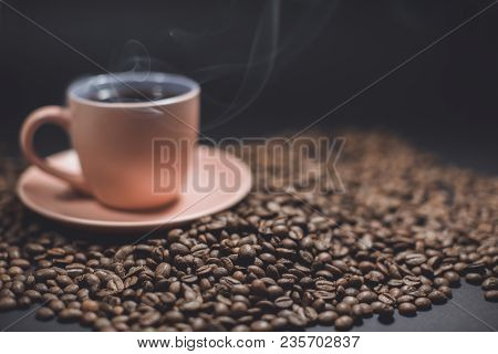 Cup Of Black Steaming Coffee On A Spilled Roasted Coffee Beans On A Black Background.