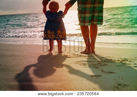 Silhouette Of Father And Little Daughter Walk At Sunset Beach
