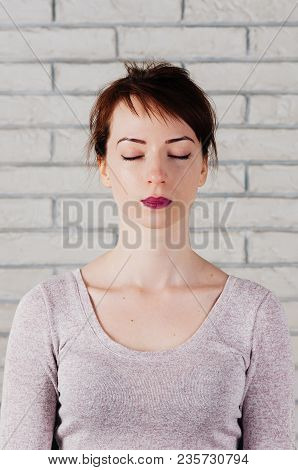 A Pretty Girl With Eyes Closed As In Meditation, Peaceful Look, With White Brick Wall In The Backgro