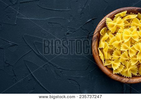 Farfalle Raw Pasta In A Wooden Bowl On A Black Textured Background From The Side. Close-up With The 