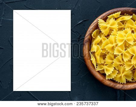 Farfalle Raw Pasta In A Wooden Bowl On A Black Textured Background From The Side. Close-up With The 