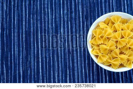 Farfalle Raw Pasta In A White Bowl On A Striped White Blue Cloth Background With A Side. Close-up Wi