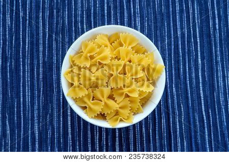Farfalle Raw Pasta In A White Cup On A Striped White Blue Cloth Background In The Center. Close-up W