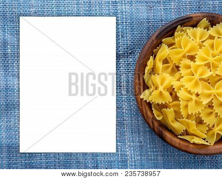 Farfalle Raw Pasta In Wooden Bowl On Blue Knitted Textured Background With Side. Close-up With The T