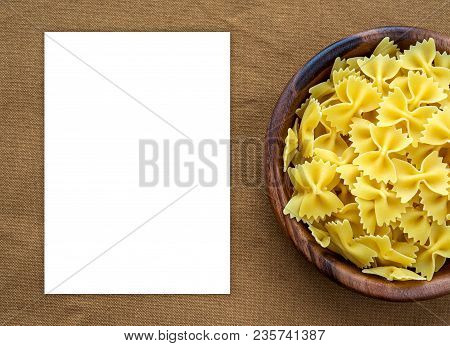 Farfalle Raw Pasta In A Wooden Bowl On A Brown Rustic Background Texture With A Side. Close-up With 