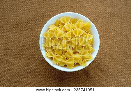 Farfalle Raw Pasta In A White Cup On A Brown Rustic Texture Background, In The Center Close-up From 