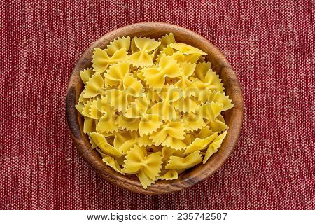 Farfalle Raw Pasta In A Wooden Bowl On A Red Brown Rustic Texture Background, In The Center Close-up