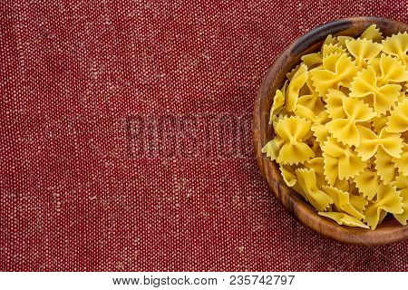 Farfalle Rawpasta In A Wooden Bowl On A Red Brown Rustic Texture Background With A Side. Close-up Wi