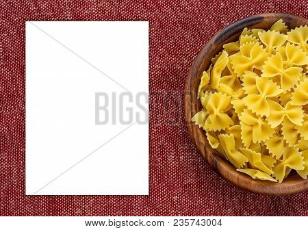 Farfalle Rawpasta In A Wooden Bowl On A Red Brown Rustic Texture Background With A Side. Close-up Wi