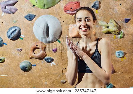 Woman Climber Preparing To Climb Indoors In Bouldering Gym With Dramatic Light. Woman Using Chalk