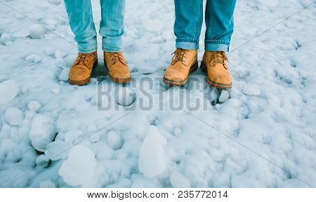Couple In A Brown Hiking Boots And Blue Jeans Stand On Ice. Iceland. Copy Space