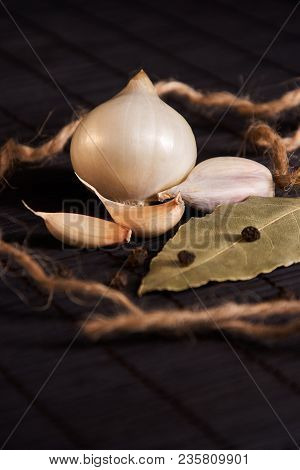 Onion, Garlic, Black Pepper And Bay Leaf On A Black Table