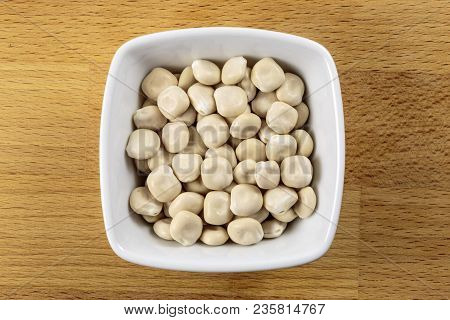 Overhead Shot Of Raw Lupini Beans In A White Bowl On A Wooden Chopping Board Background