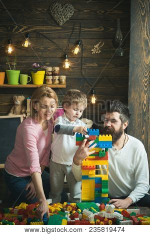 Family Spend Time Together In Playroom. Parents Help Cute Son To Make A House Out Of Plastic Blocks.