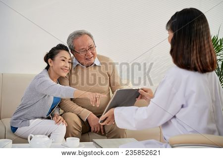 General Pratitioner Showing Medical Tests Results To Aged Vietnamese Couple