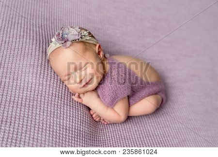 Little newborn baby girl in purple bodysuit smiling while sleeping