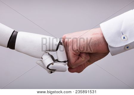 Robot And Human Hand Making Fist Bump On Grey Background