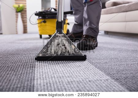 Low Section Of A Person Cleaning The Carpet With Vacuum Cleaner In Living Room