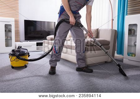 Low Section Of A Person Cleaning The Carpet With Vacuum Cleaner In Living Room