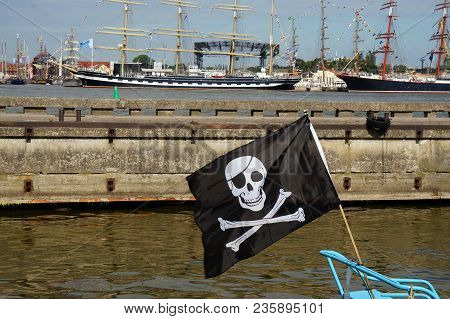 Black Pirate Flag Flying Form The Top Of A Mast On A Boat In The Port