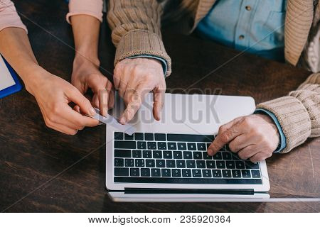 Close-up View Of Woman Helping Senior Man Using Laptop And Credit Card