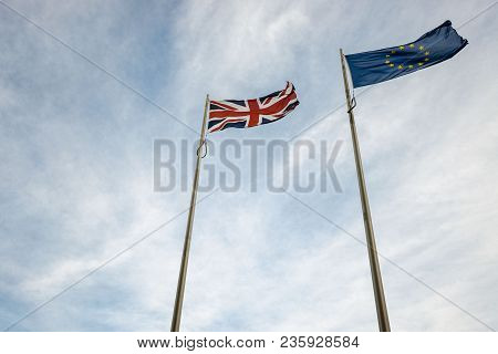 Looking Up At Eu And Uk Flags Blowing In The Wind With Blue Sky