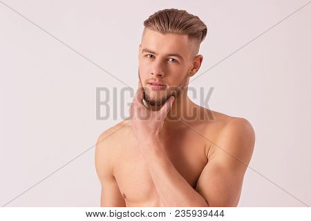 Handsome thoughtful man touching his chin and looking to camera while standing isolated on white background. Pensive naked hipster model posing to camera. Masculinity and charisma of bearded hipster