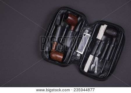 Different Smoking Tobacco Pipes, Tobacco Tamper And Lighter In A Black Leather Bag On Dark Backgroun