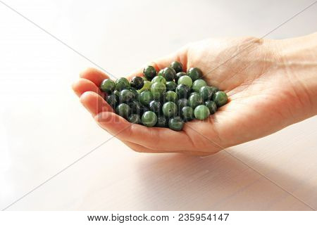 Natural Green Jade Nephrite Mineral Stones Beads. The Green Jade Stone Lies In The Hands. Hands Hold
