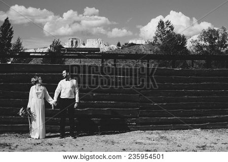The Bride In The Groom Poses In Front Of The Wooden Fence