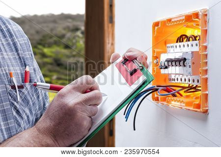 Electrician Technician At Work On A Residential Electric Panel, He Writes On The Notepad