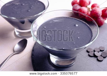 Black Yogurt With Activated Carbon And Grapes On A White Background.