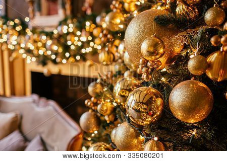 Christmas Background With Illuminated Fir Tree With Golden Decpration And Fireplace In Living Room.