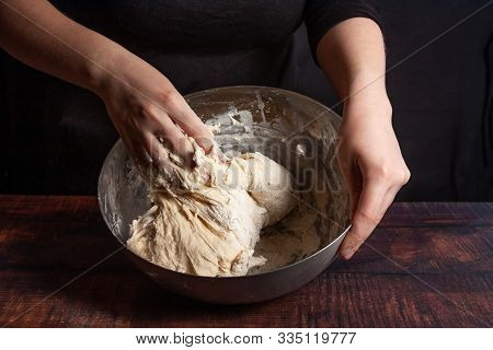 A Cook In Black Kneads The Dough In A Metal Bowl For Cooking Bread In The Kitchen.