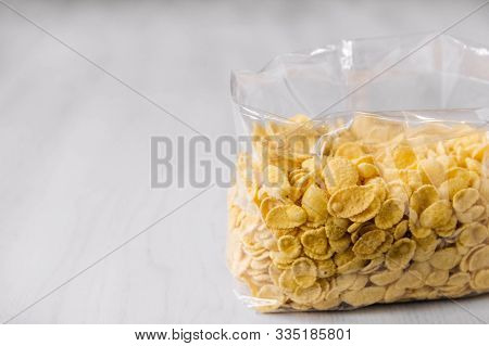 Cornflakes In Plastic Bag On White Wooden Surface. Place For Your Text