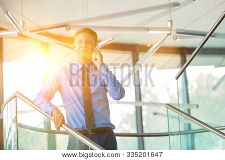 Young attrctive businessman talking on smartphone in office with lens flare