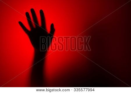Silhouette of a female hand through glass on a red background. Horror concept