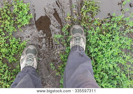 Top View On Men Feet Wearing Sneakers Standing On Miry Earth Road