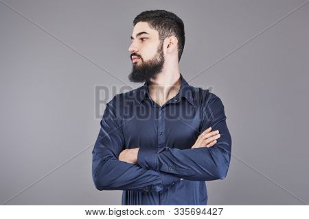 Young Handsome Man With A Beard Leaning Against Grey Wall With Arms Crossed. Copy Space.